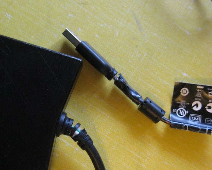 A USB cable split just behind its plug and patched with tape.