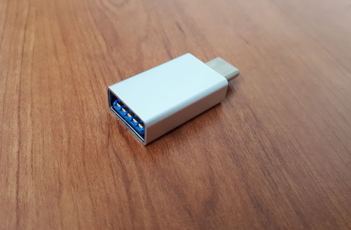 A small silver USB-C to USB-A adapter lying on a wooden desk.