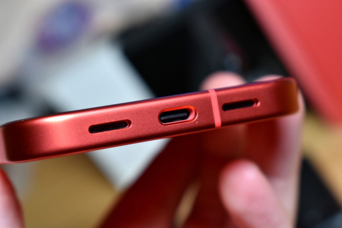Close-up of the USB-C charging port on the bottom edge of a red phone, held between finger and thumb.