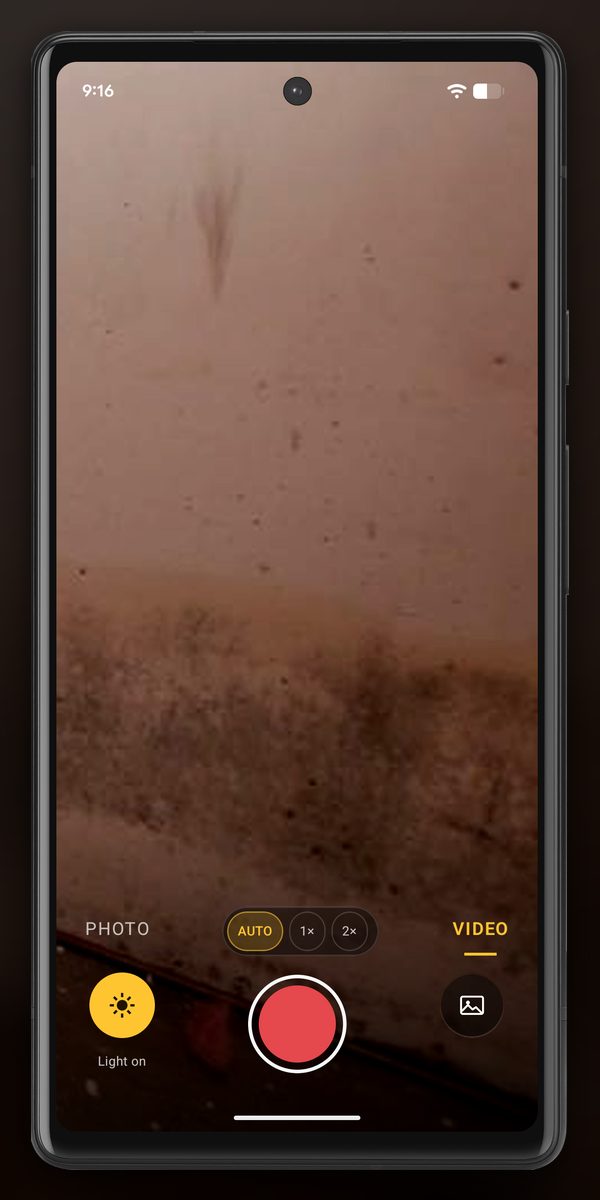 InspectCam in VIDEO mode on an Android phone, pointed close at the lower part of a flooded basement wall: a dark band of waterline staining and mold runs across the screen above the controls. Light on is lit at the bottom left, with the red record button and the AUTO, 1x and 2x zoom chips.