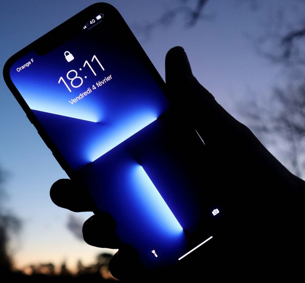 An iPhone held up at dusk showing its lock screen, with the flashlight button at the bottom left and the camera button at the bottom right.