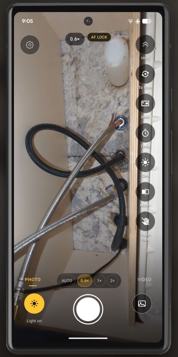 A real InspectCam screenshot under a sink, in a phone frame: the supply hoses and shut-off valves lit by the phone's light.