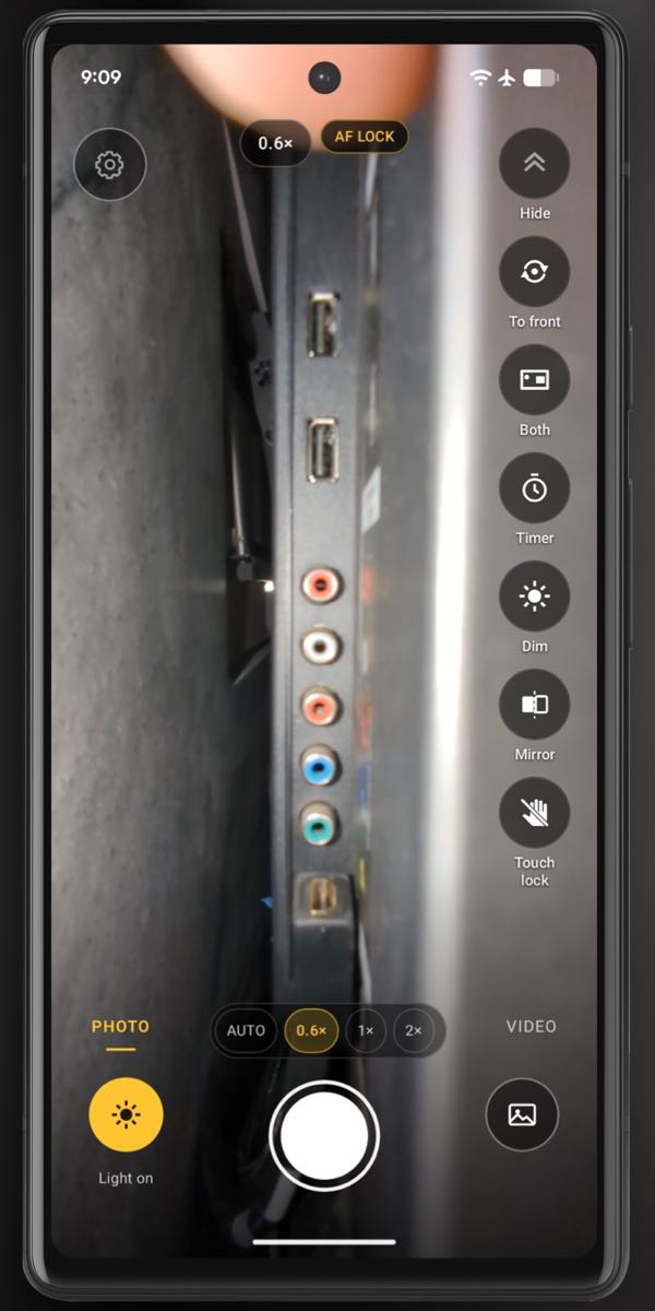 A real InspectCam screenshot behind a wall-mounted TV, in a phone frame: the row of ports on its back lit by the phone's light.