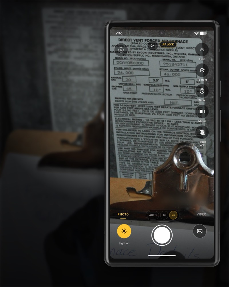 InspectCam’s camera held up to a furnace rating plate on a clipboard. On the screen the MODEL NO. and SERIAL NO. boxes, the BTU input and output and the electrical rating are all readable, with 2× zoom selected and the yellow Light on button lit.