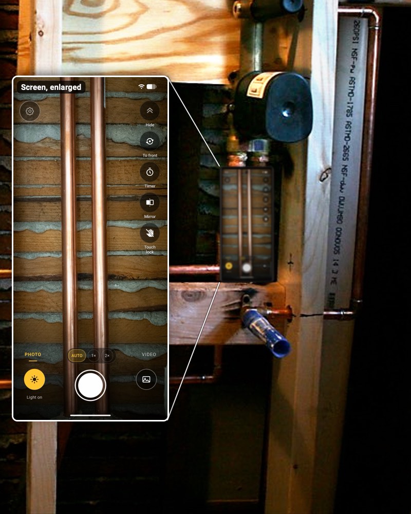 A phone running InspectCam standing on a wood block in an open stud bay.