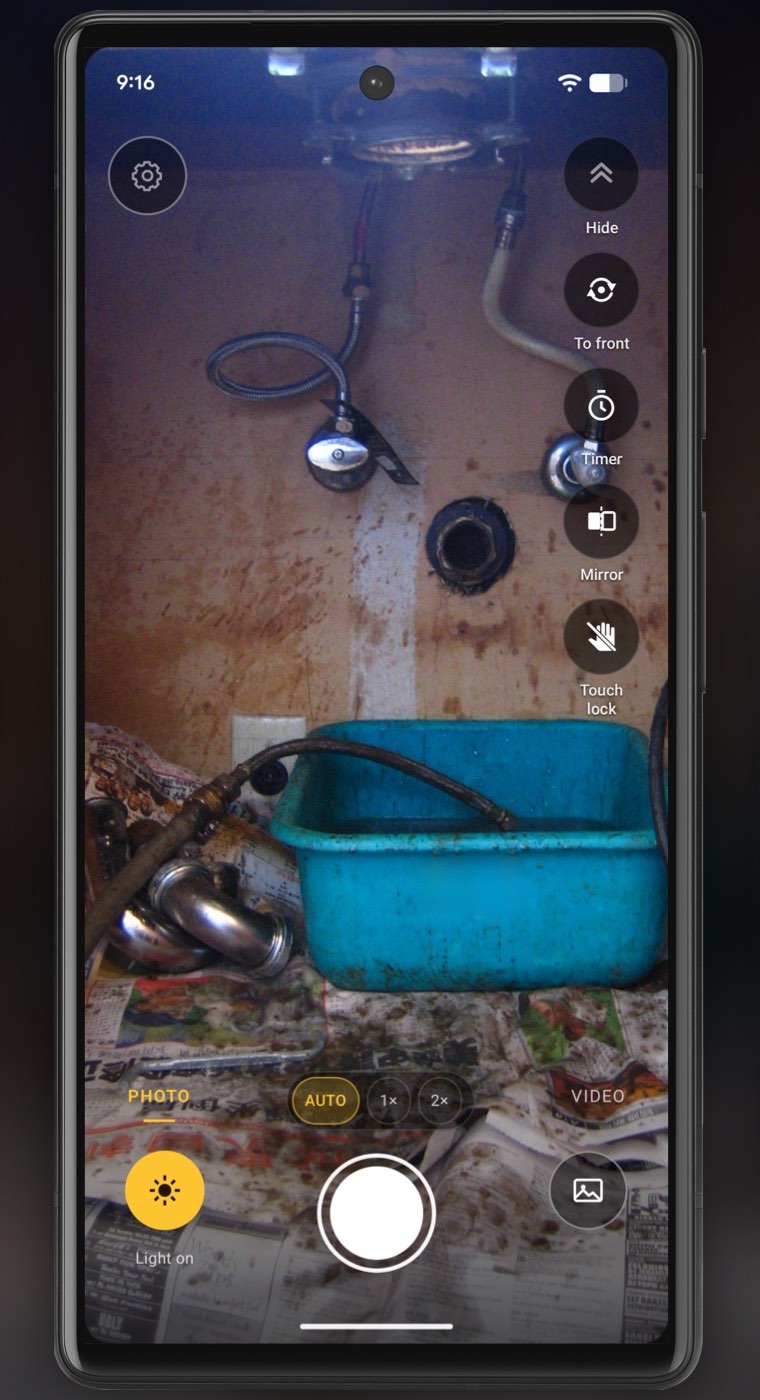 The same view under the sink in InspectCam with the light on: braided supply hoses, two chrome shut-off valves, the drain opening in the wall and a blue plastic tub, all clearly lit, with Light on lit at the bottom left.