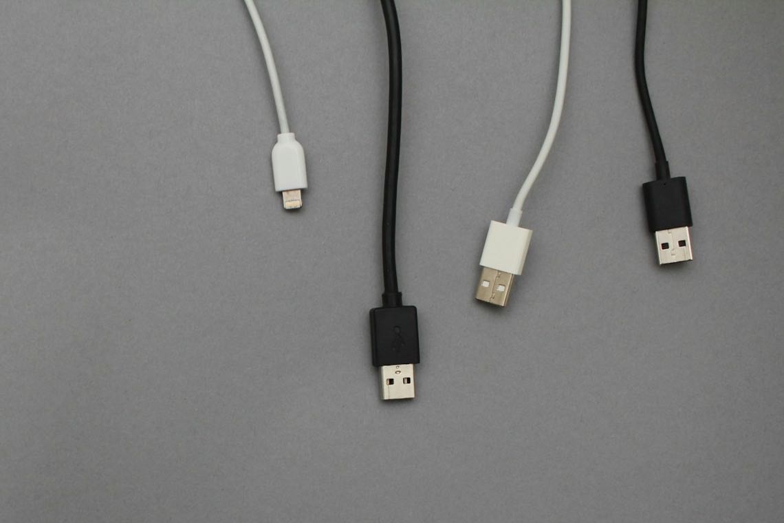 Four charging cables hanging side by side against a grey background, three of them ending in identical-looking USB-A plugs.