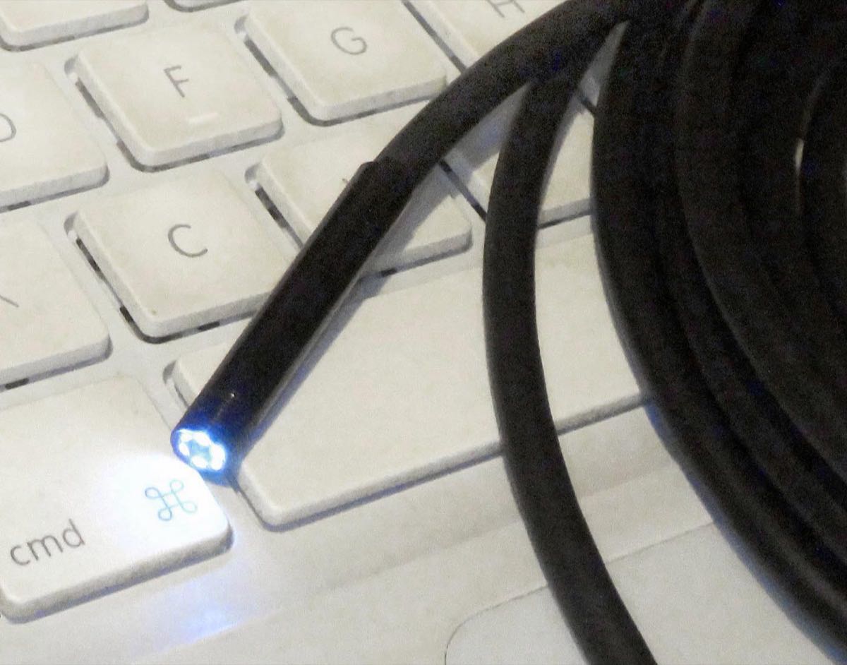 The camera tip of a phone borescope, lit by its own small LEDs, on the end of a long black cable coiled on a laptop keyboard.