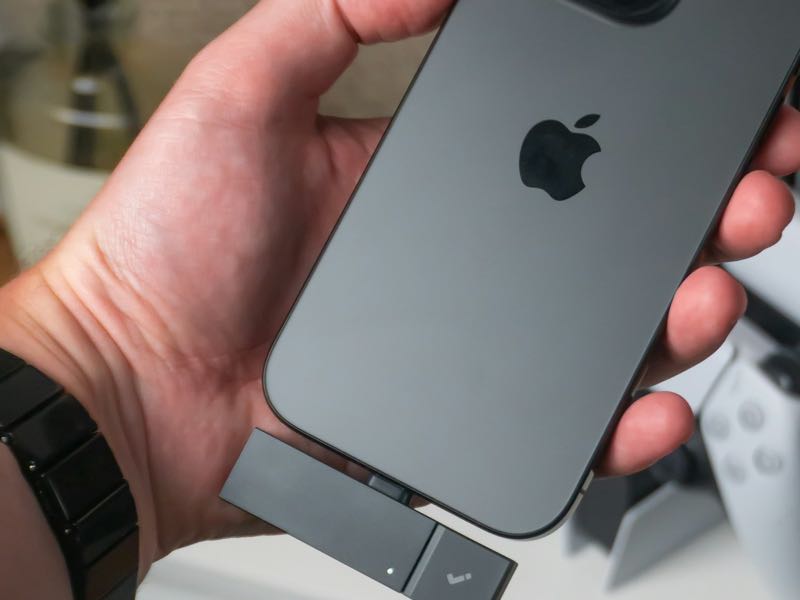 The back of an iPhone held in a hand, with a small USB-C accessory plugged into its USB-C port.
