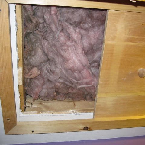 An attic hatch slid open in a ceiling, with pink fiberglass insulation behind it.