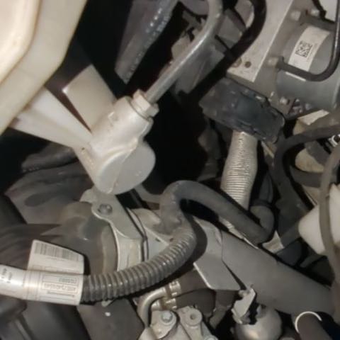 Deep in an engine bay: hoses, a metal bracket and a sticker on a part, lit by the phone light.