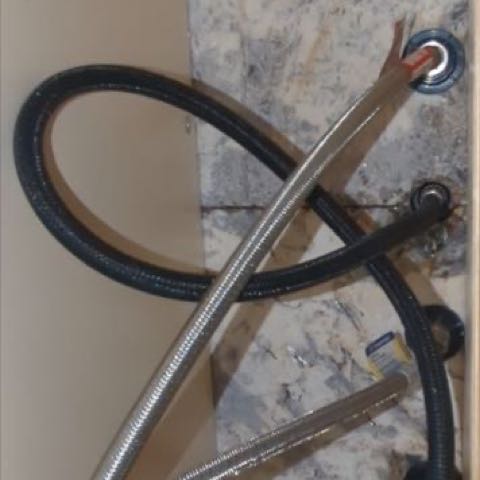 Under a kitchen sink: braided supply lines and a black drain hose running up to the cabinet floor.