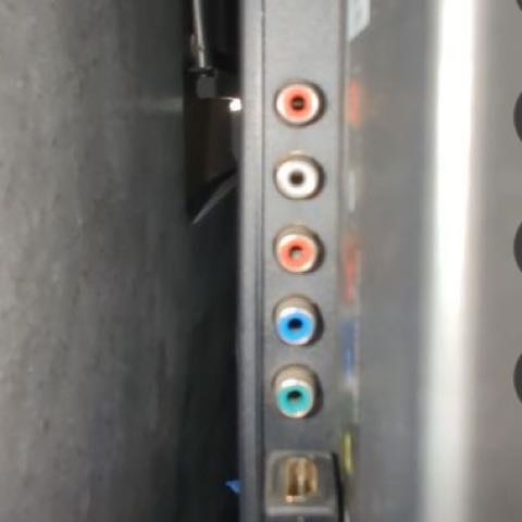 The back of a wall-mounted TV lit by a phone light: a column of colored audio and video ports and an HDMI port.