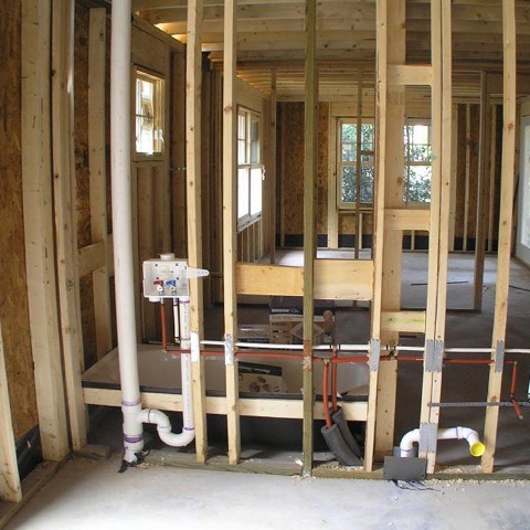 An open stud wall before the drywall: a washer box with its two valves, white drain pipes and red and white supply lines running through the studs.